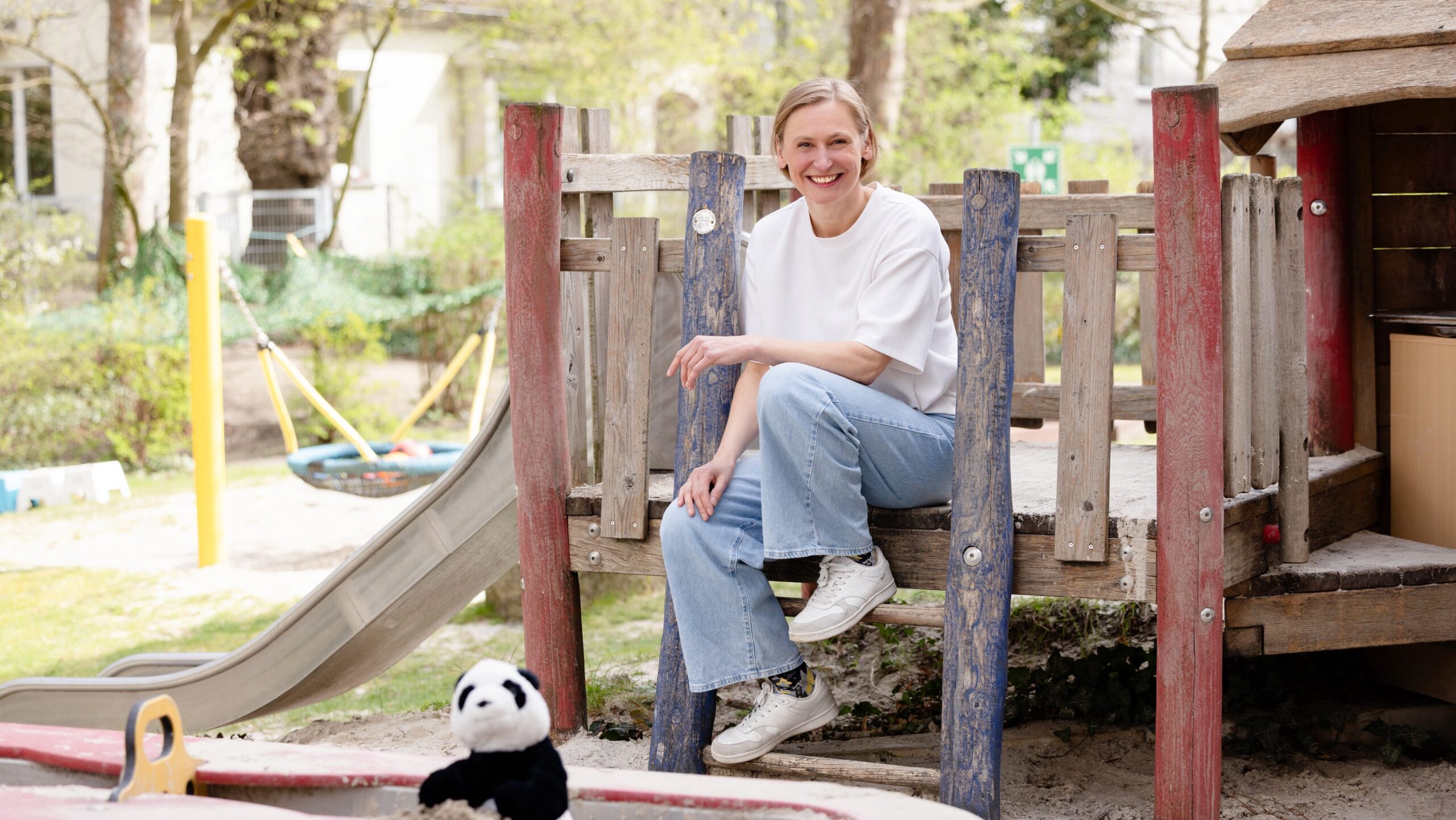 Eine blonde Frau sitzt auf einem Kinderspielplatz.