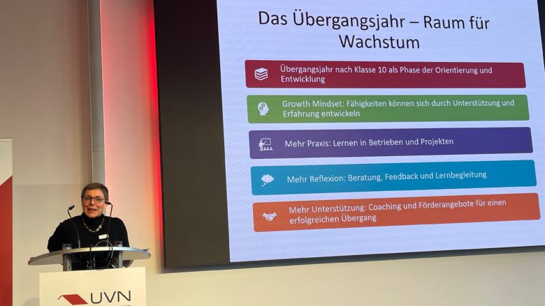 Eine Frau mit kurzen grauen Haaren hält einen Vortrag mit Präsentation.