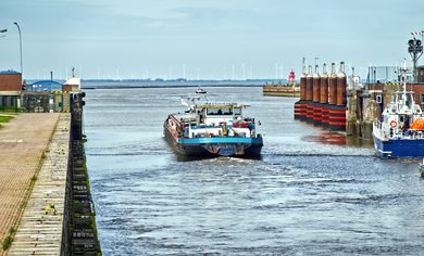Inland vessel exiting the large lock in emden, moving into the expansive ems dollart estuary with a distant wind power park