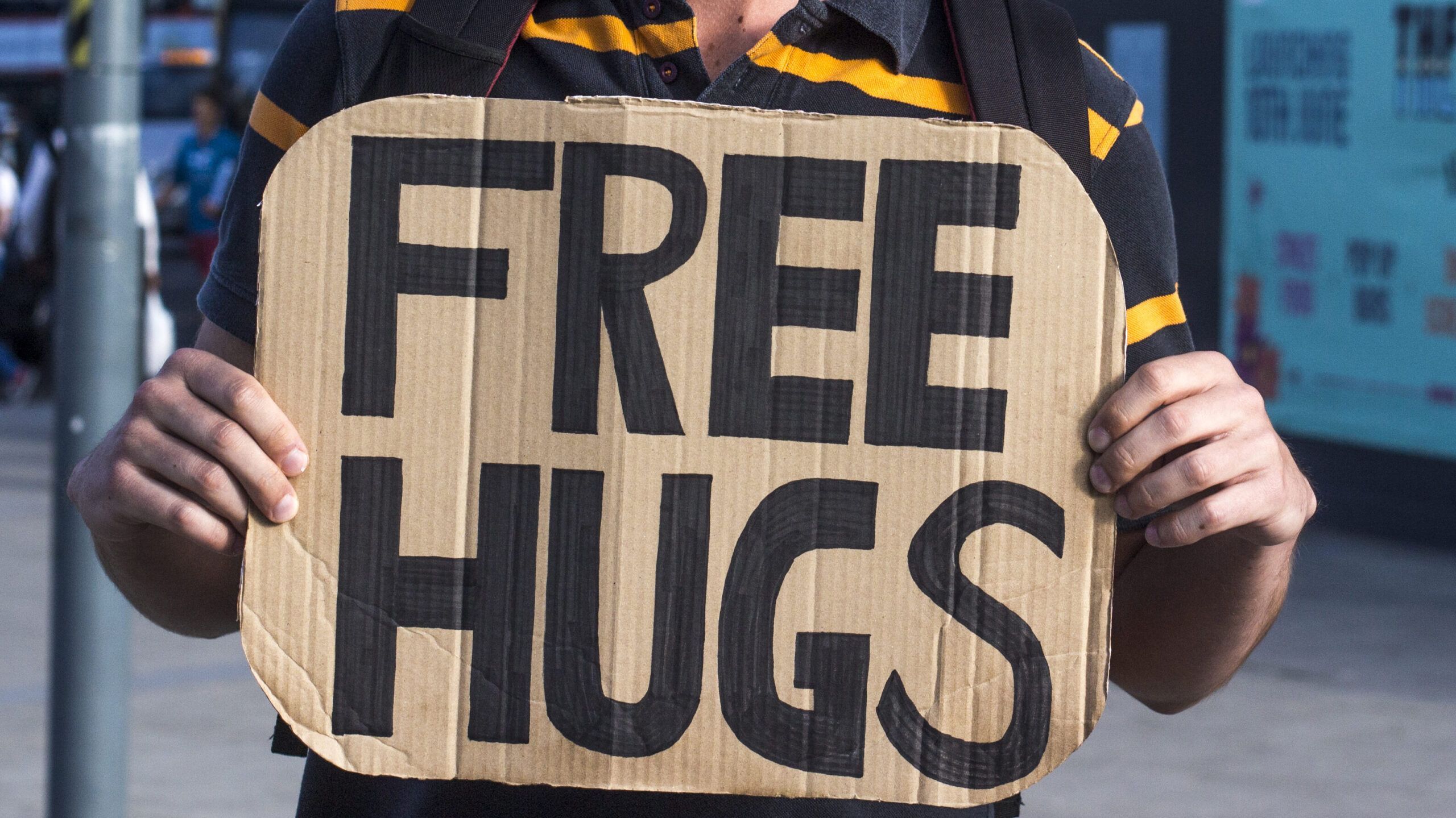 Man holding a cardboard sign with free hugs written on it