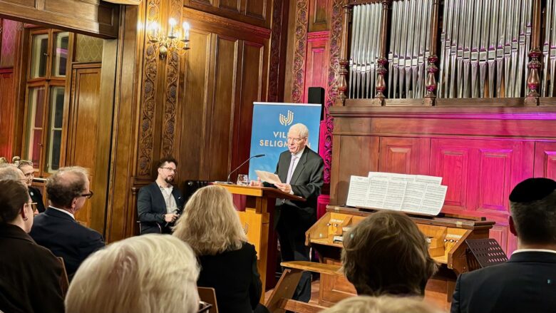 Ein weißhaariger Mann spricht vor Publikum, hinter ihm eine Orgel.