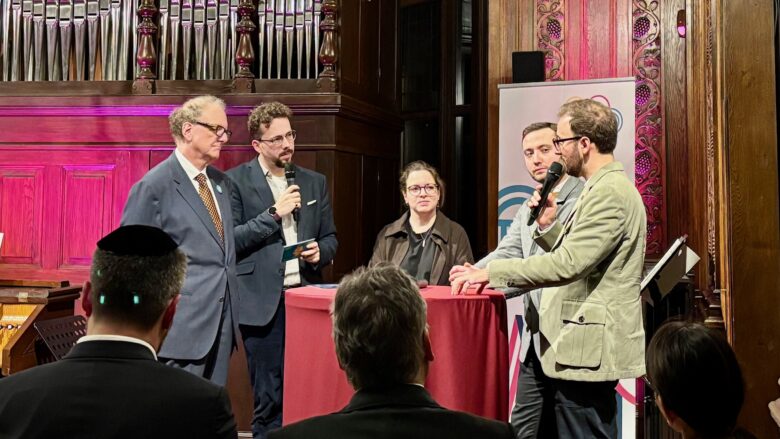 Fünf Personen diskutieren vor Publikum an einem Stehtisch, dahinter eine Orgel