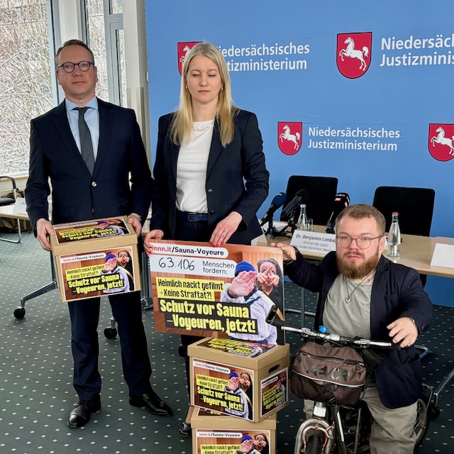 Drei Personen präsentieren Plakate mit der Aufschrift "Schutz vor Sauna-Voyeuren, jetzt!"