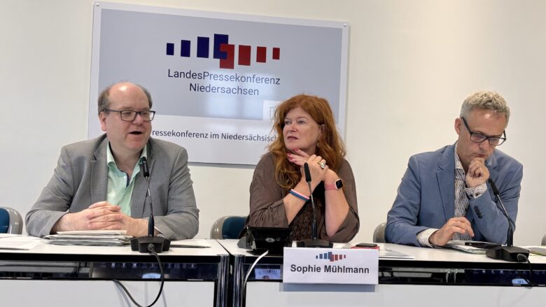 Drei Personen auf dem Podium der Landespressekonferenz. Minister Meyer spricht und hat die Hände verschränkt.