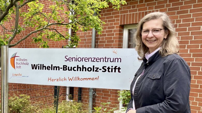 Eine Frau mittleren Alters steht lächelnd vor dem Eingang.