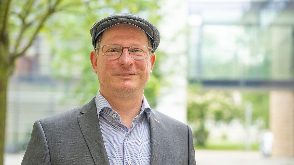 Ein Porträtfoto zeigt einen Mann mit Brille und Schiebermütze.
