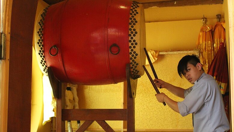 Ein Teenager trommelt auf einer riesigen Trommel, die auf einem Gerüst auf der Höhe seines Kopfes steht.