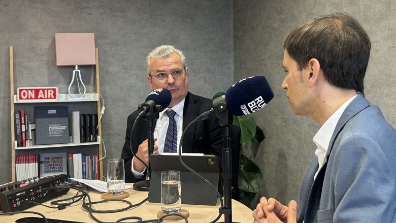 Zwei Männer sitzen vor Mikrofonen und diskutieren.