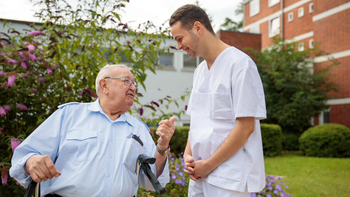 Altenpfleger im Gespräch mit einem alten Herrn mit Rollator