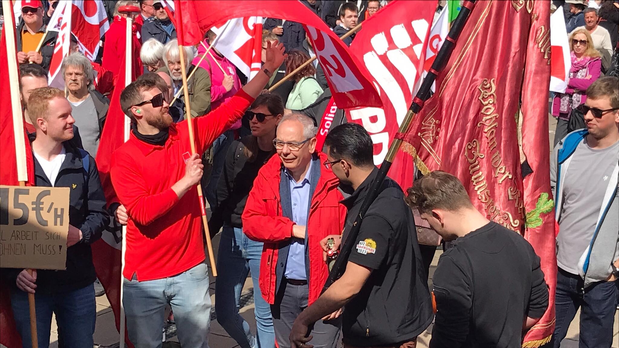 Junge Gewerkschafter demonstrieren mit roten Fahnen. In der Mitte ein älterer Mann in roter Jacke.